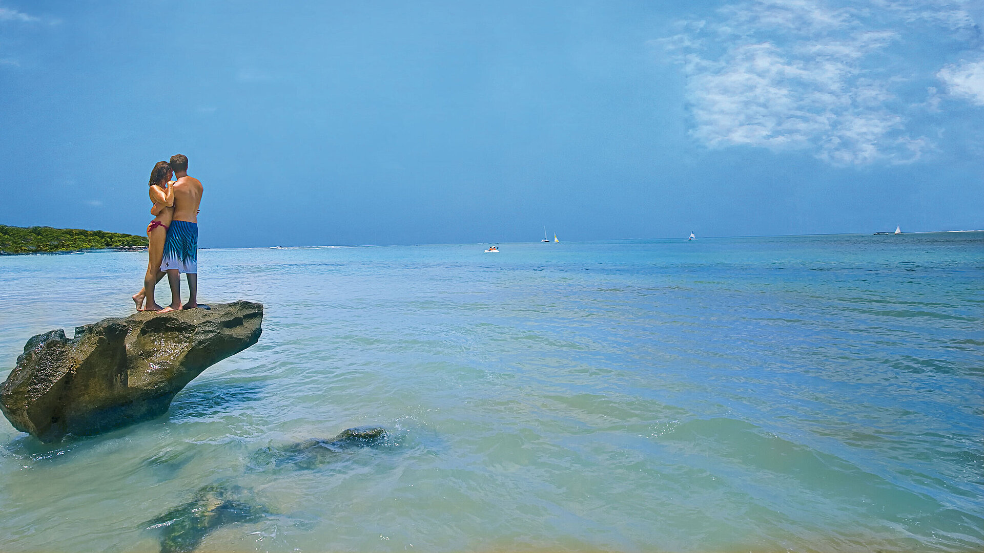 Strand von Mauritius Paar steht romantisch auf Felsen im türkisblauen Meer unter blauem Himmel