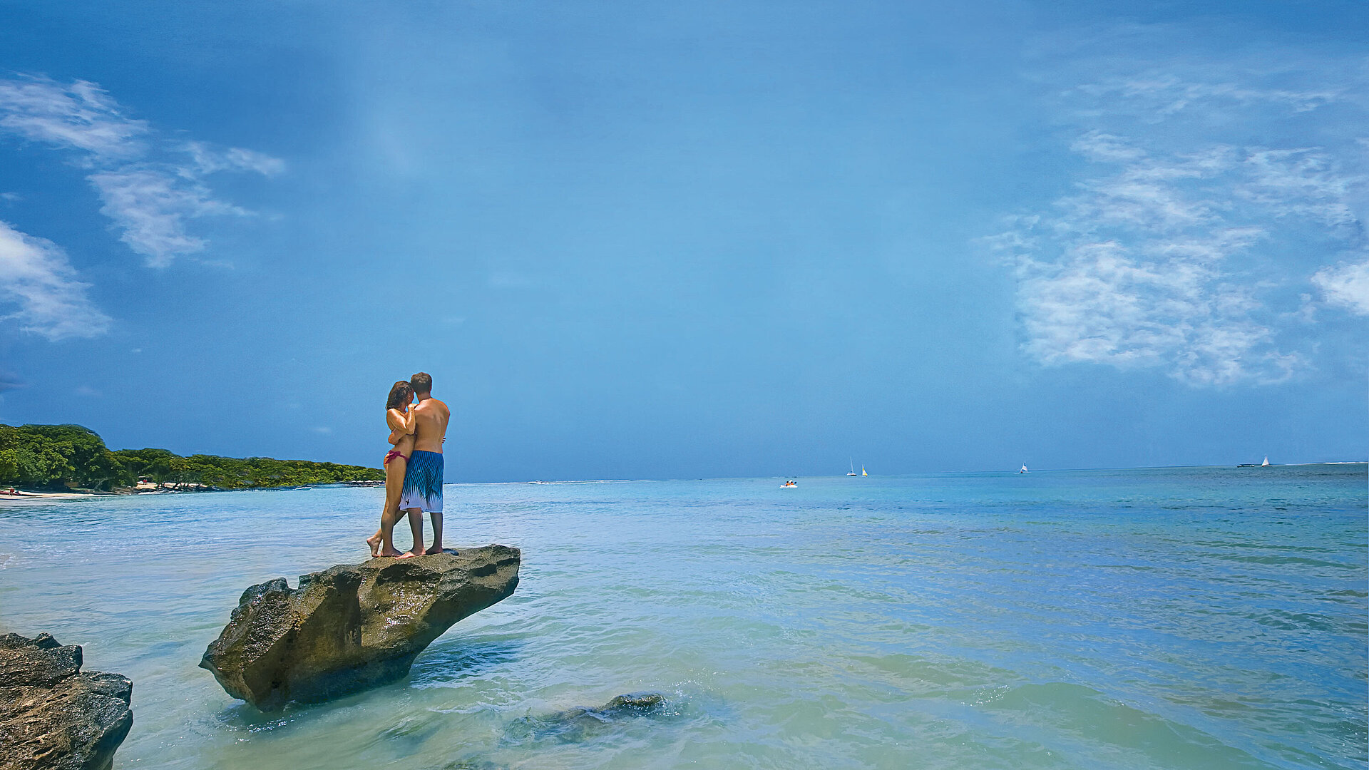 Strand von Mauritius Paar steht romantisch auf Felsen im türkisblauen Meer unter blauem Himmel