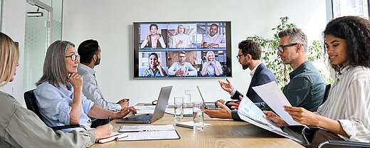 © insta photos - AdobeStock.com Geschäftsteam in Videokonferenz mit Kollegen auf großem Bildschirm