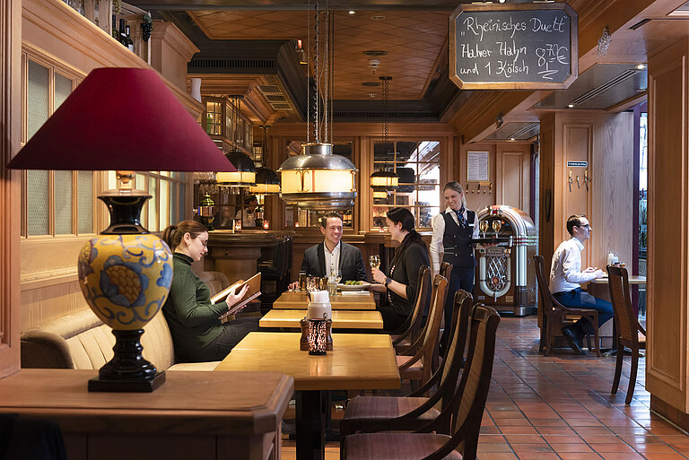Bier- und Weinstube "Kölsche Stuff" Gäste in der "Kölsche Stuff" genießen Essen und Getränke in gemütlicher Atmosphäre mit rustikalem Dekor.