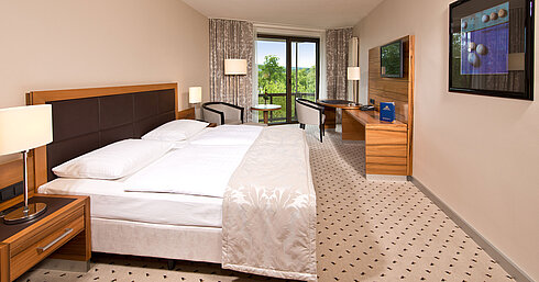 Comfort Zimmer Helles Zimmer im Maritim Hotel Bad Homburg mit gemütlichem Bett, Schreibtisch und Balkon mit grünem Ausblick.