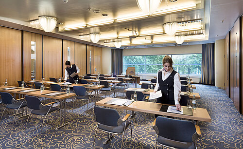 Saal Maritim II Parlament Mitarbeiterinnen bereiten einen Tagungsraum im Maritim Hotel Frankfurt mit Reihenbestuhlung und Blick ins Grüne vor.