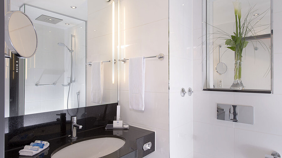 Badezimmer Helles Bad mit Glasdusche, Spiegel und schwarzer Ablage im Maritim Hotel München