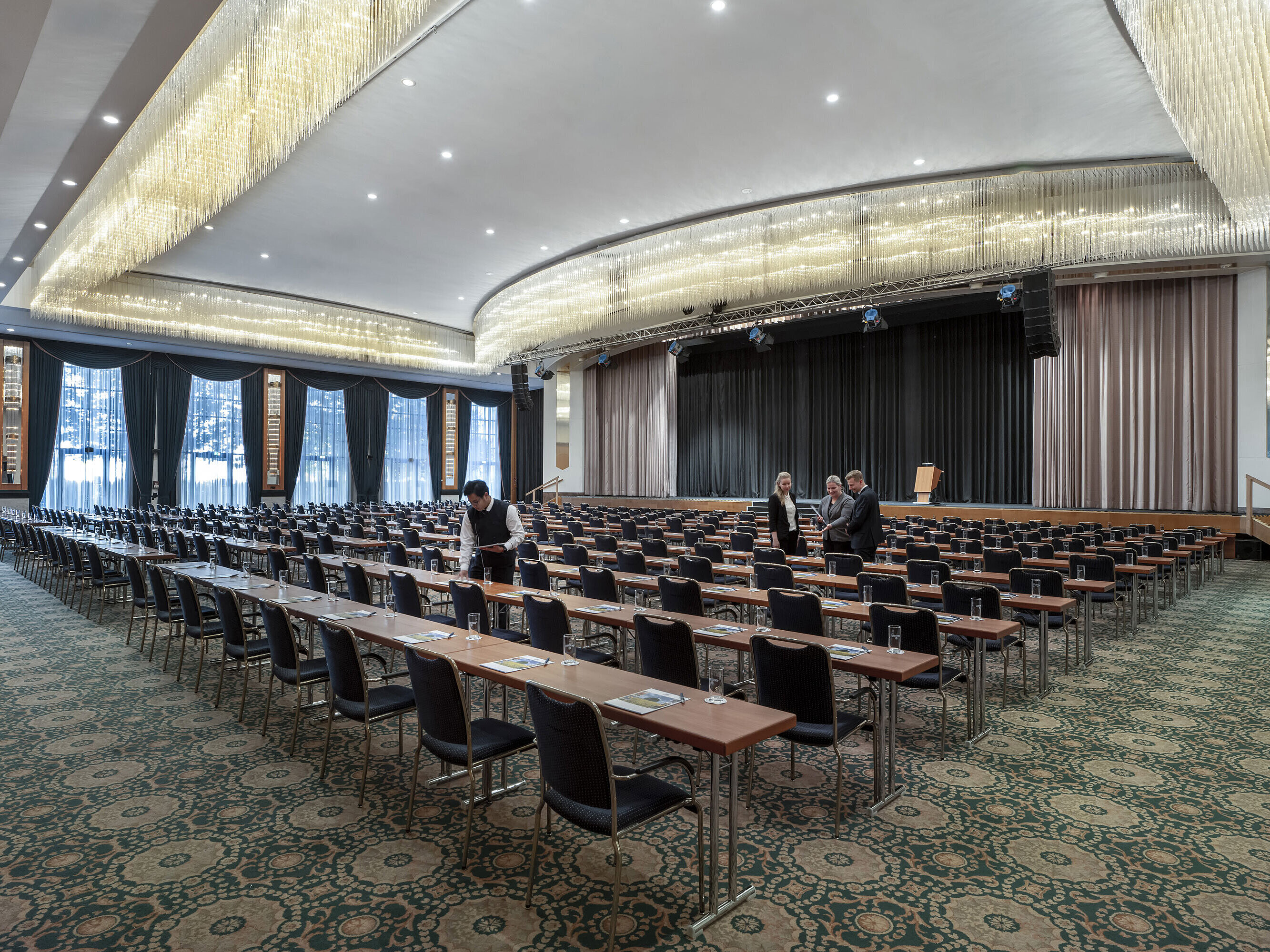 Saal Maritim Prächtiger Saal im Maritim Hotel Magdeburg mit Bühne, Reihenbestuhlung und luxuriösem Kronleuchter.