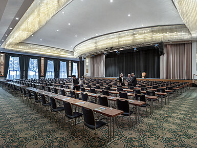 Saal Maritim Prächtiger Saal im Maritim Hotel Magdeburg mit Bühne, Reihenbestuhlung und luxuriösem Kronleuchter.