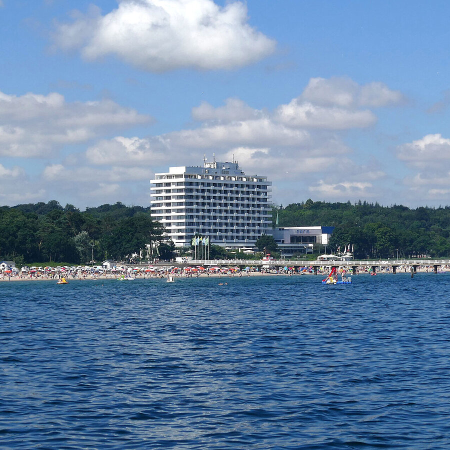 Außenansicht Maritim Seehotel Timmendorfer Strand, Seebrücke und bunte Flaggen vom Boot aus bei sonnigem Wetter.