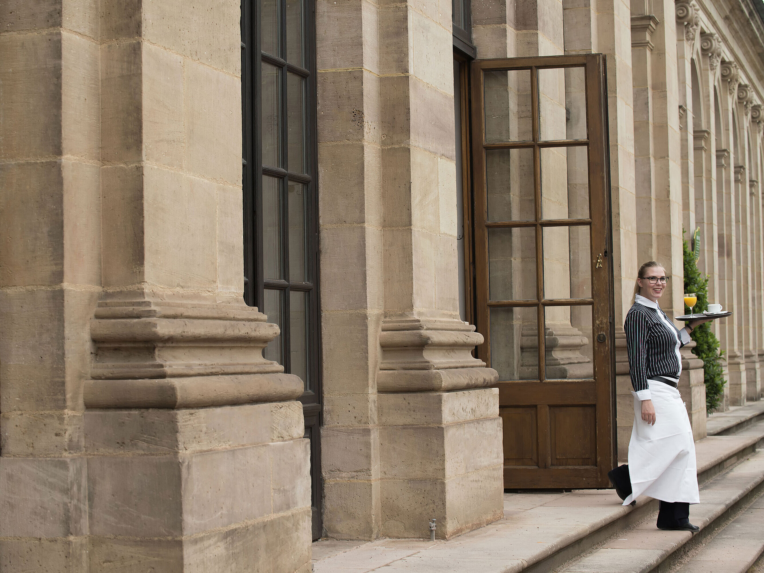 Maritim Service Freundliche Servicekraft serviert Frühstück mit frisch gepresstem Orangensaft auf der Terrasse des Maritim Hotel Fulda.
