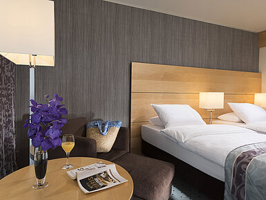 Classic Zimmer Classic Zimmer im Maritim Hotel Düsseldorf mit elegantem Doppelbett, gemütlicher Sitzecke, frischer Blume und Lesematerial.