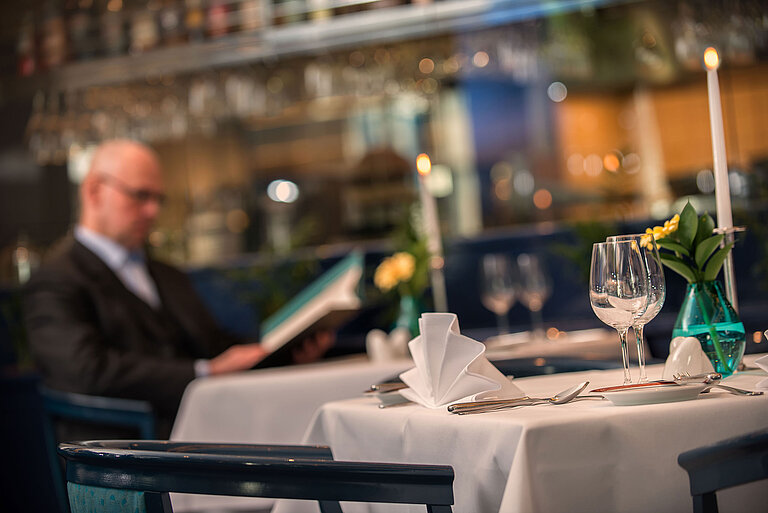 Detailansicht Restaurant Eleganter gedeckter Tisch im Restaurant des Maritim Hotel Magdeburg mit einem Gast beim Studieren der Speisekarte.