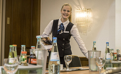 Salon Lenné Freundliche Servicemitarbeiterin im Salon Lenné des Maritim Hotels Bonn mit Getränken und Tagungsunterlagen auf dem Tisch.
