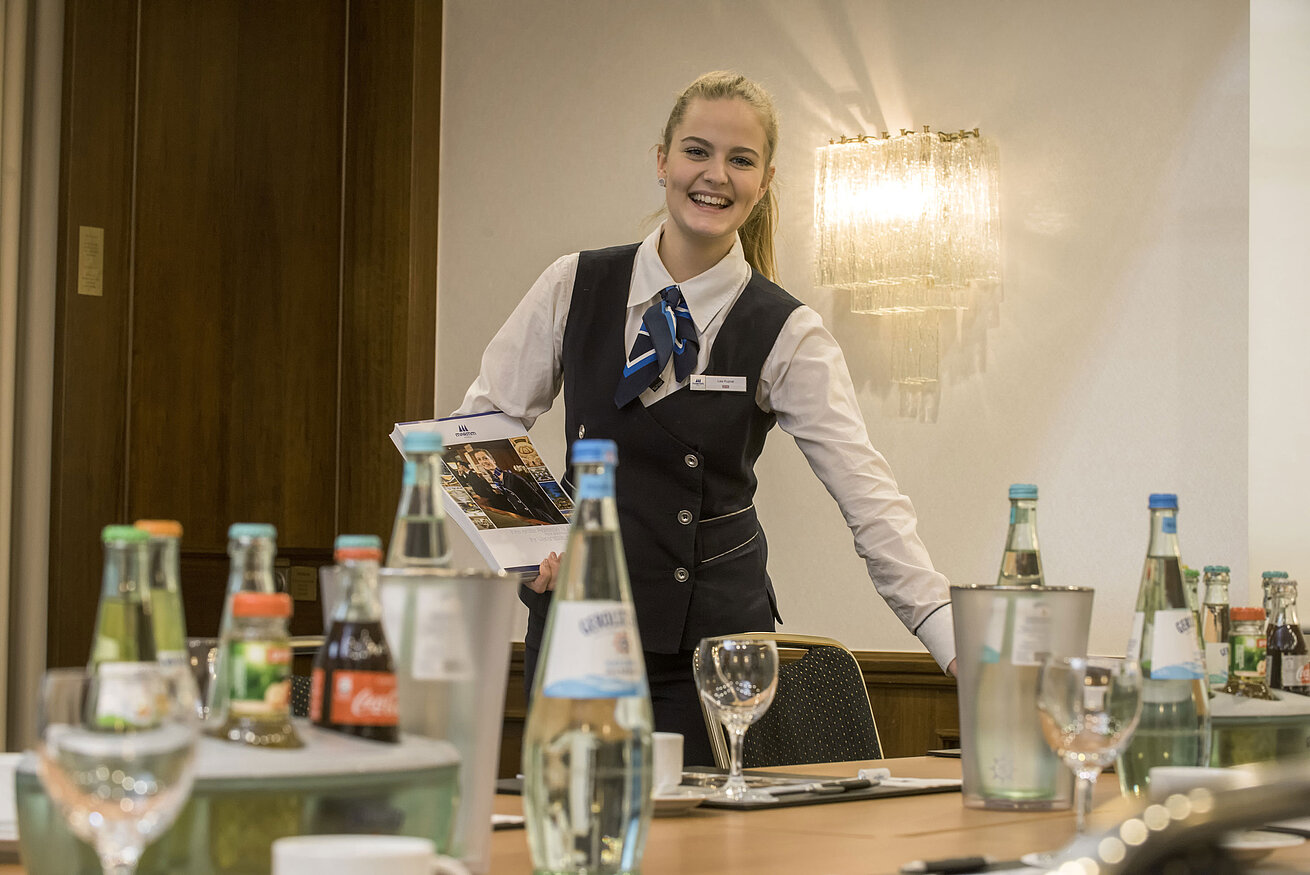 Salon Lenné Freundliche Servicemitarbeiterin im Salon Lenné des Maritim Hotels Bonn mit Getränken und Tagungsunterlagen auf dem Tisch.