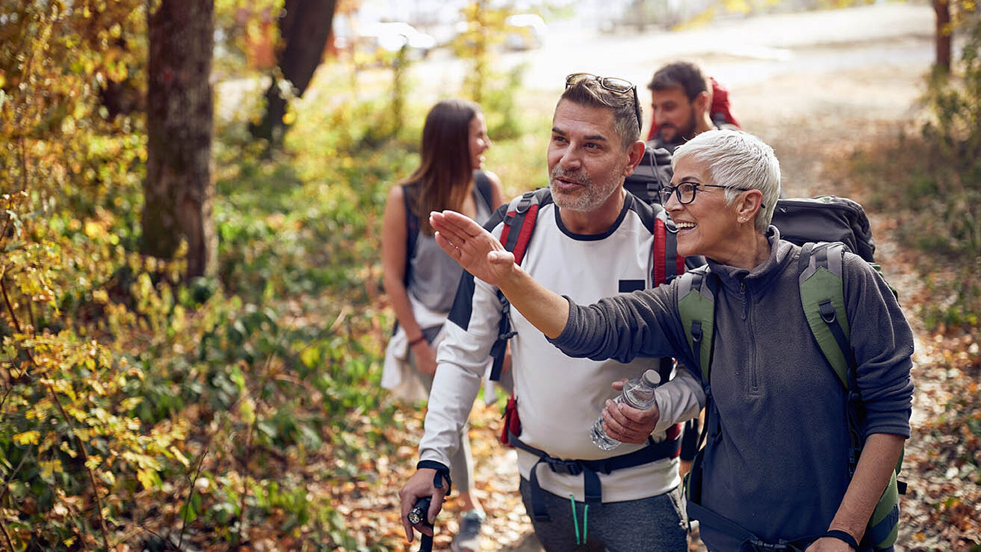 © luckybusiness - AdobeStock.com Fröhliche Wandergruppe im Wald, Frau zeigt Richtung während der Herbstwanderung. Titel: Gemeinsame Wanderung