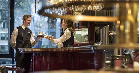 Café "Brasserie" Freundliches Servicepersonal an der Bar der Brasserie im Maritim Hotel Bonn, das Getränkeservice mit einem Lächeln anbietet.
