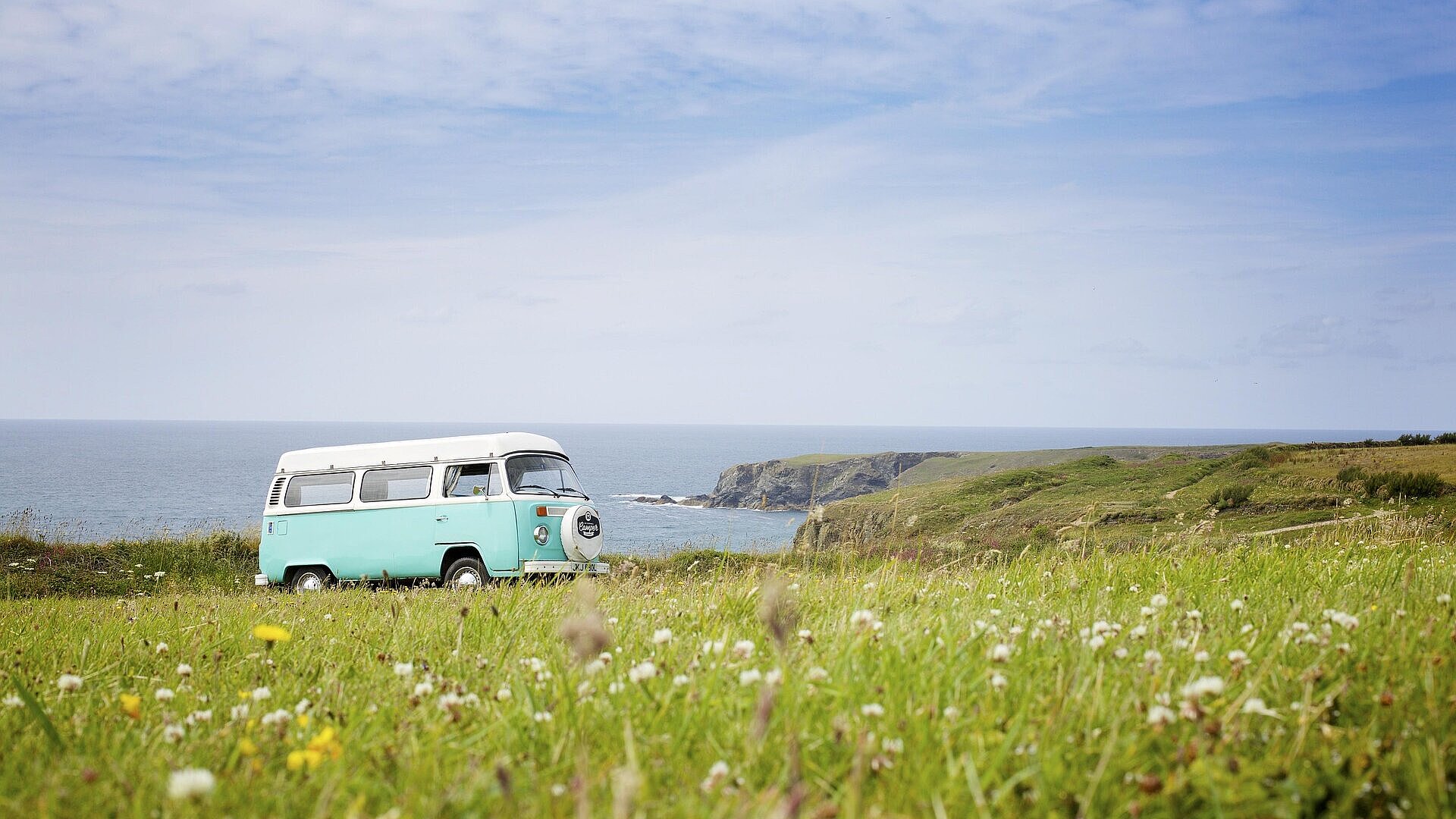 VW-Bus auf Reisen Retro-VW-Bus auf einer Wiese mit Blick auf das Meer und die Küste – perfekter Start ins nächste Abenteuer