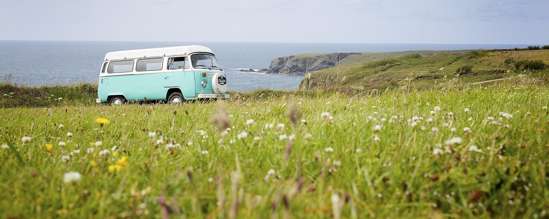 VW-Bus auf Reisen Retro-VW-Bus auf einer Wiese mit Blick auf das Meer und die Küste – perfekter Start ins nächste Abenteuer