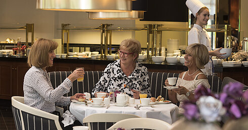 Parkrestaurant mit Sonnenterrasse Drei Frauen genießen ein entspanntes Frühstück im Maritim Hotel Bad Homburg, bedient von einer freundlichen Köchin.