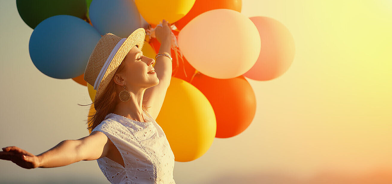 © JenkoAtaman - AdobeStock.com Frau mit bunten Luftballons im Sonnenuntergang