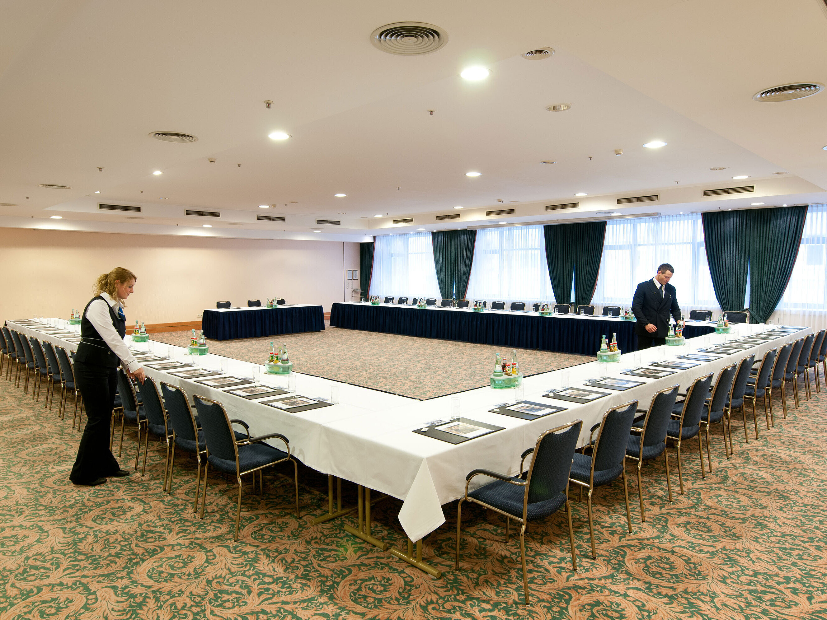 Saal Berlin Tagungsraum Saal Berlin im Maritim Hotel Magdeburg mit U-förmiger Bestuhlung, gedeckten Tischen und Vorbereitung durch das Personal.