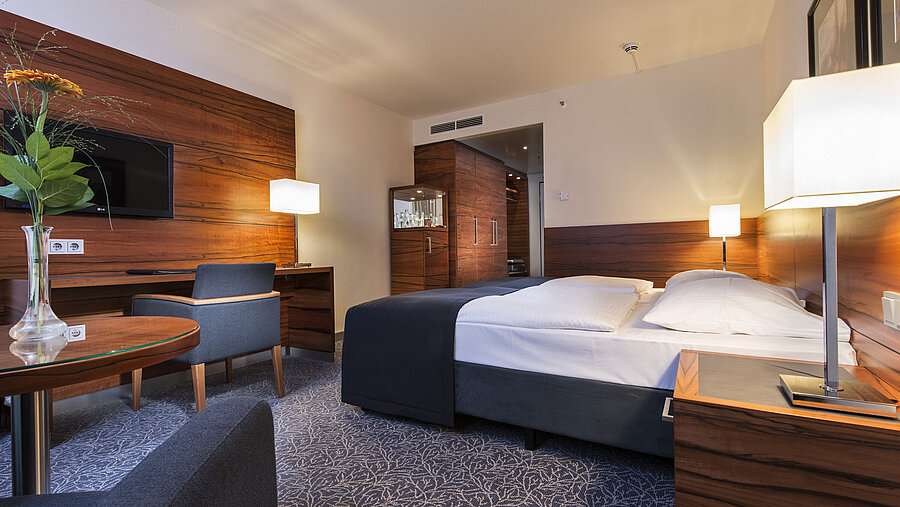 Comfort Zimmer Eingerichtetes Hotelzimmer im Maritim Hotel München mit komfortablem Bett, Arbeitsbereich, TV und Holzverkleidung.