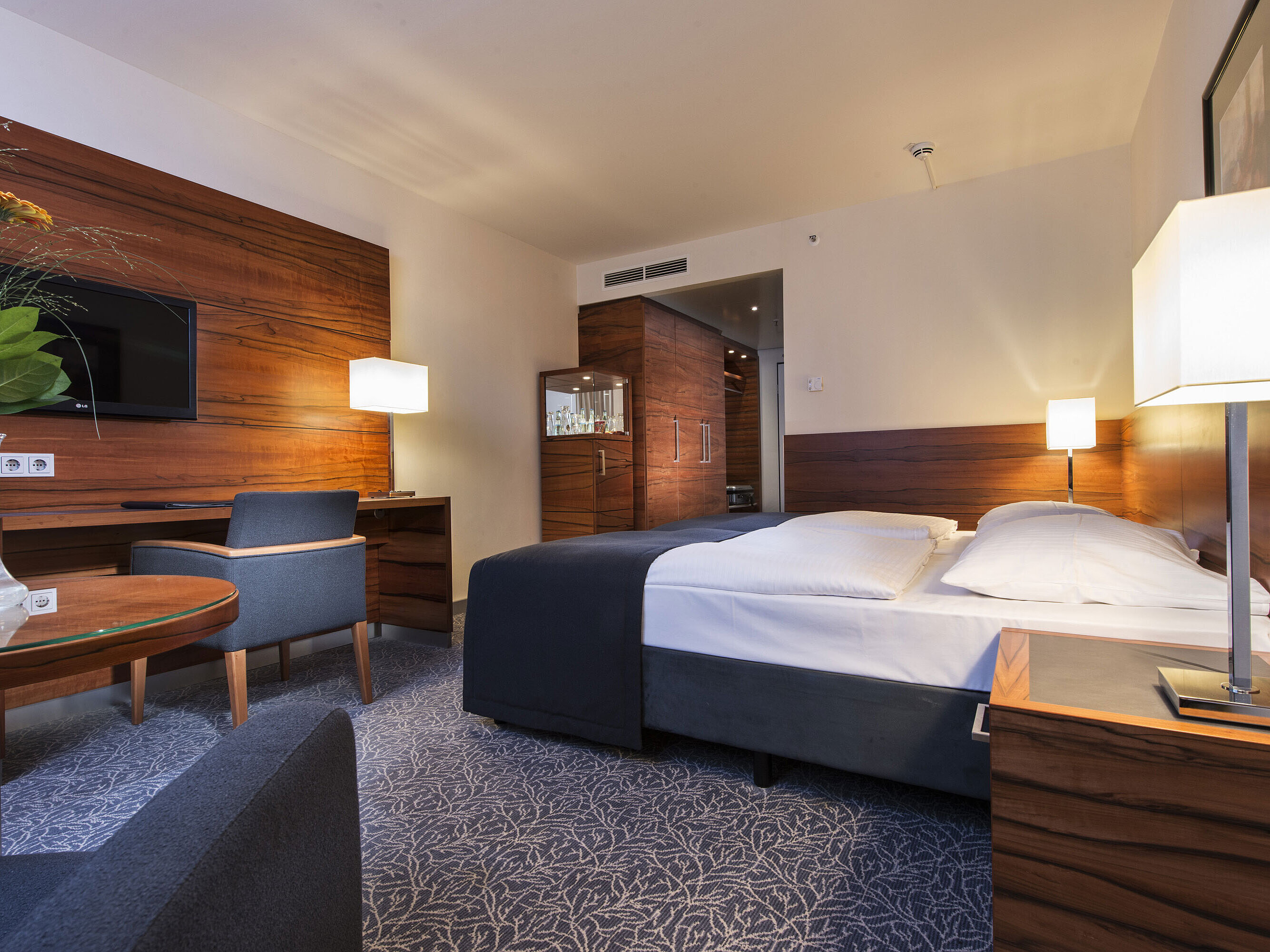 Comfort Zimmer Eingerichtetes Hotelzimmer im Maritim Hotel München mit komfortablem Bett, Arbeitsbereich, TV und Holzverkleidung.