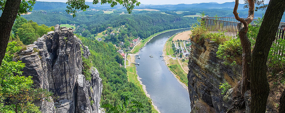 © fotografci - AdobeStock.com Aussicht von Felsen auf die Elbe in der Sächsischen Schweiz mit grünem Tal und Dorf im Sommer