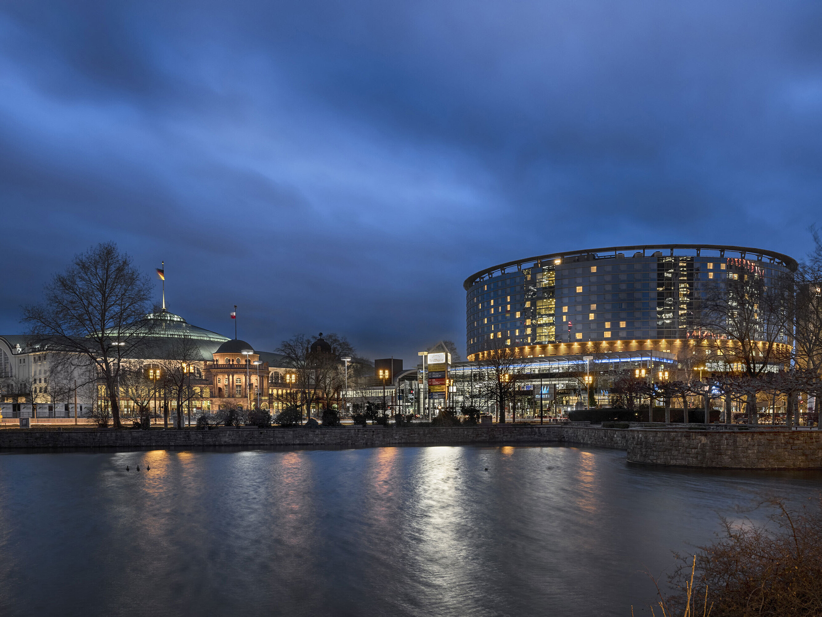 Außenansicht - Nacht Maritim Hotel Frankfurt und Festhalle bei Nacht mit beleuchteter Glasfassade und Spiegelung im angrenzenden Teich.