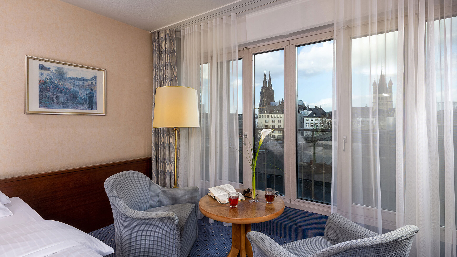 Standard Standard-Twin Zimmer im Maritim Hotel Köln mit zwei Sesseln und Tisch, großem Fenster und Blick auf den Kölner Dom.