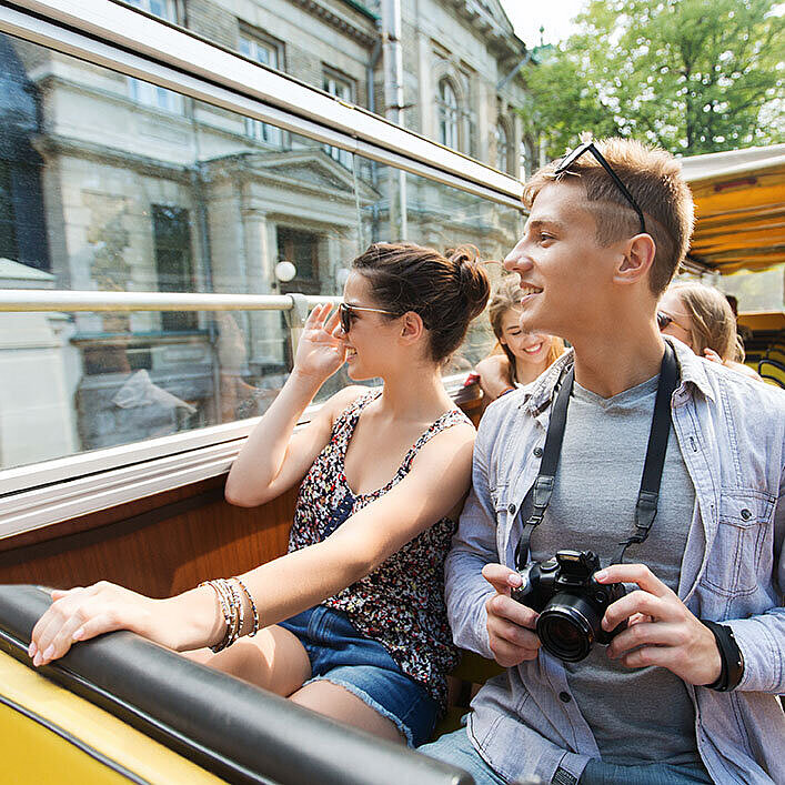 © Syda Productions – AdobeStock.com Paar im offenen Sightseeing-Bus erkundet eine Stadt und genießt den Ausblick während einer Stadtrundfahrt