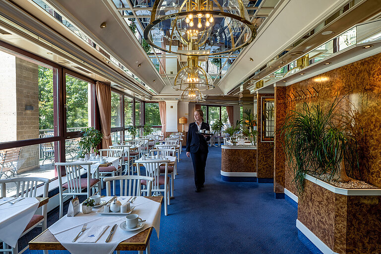 Café "Heumarkt" Restaurant im Maritim Hotel Köln mit Servicekraft und großen Fenstern mit Blick ins Grüne