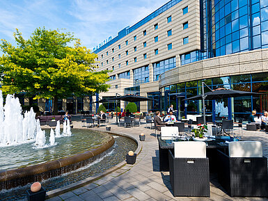 Terrasse Terrasse des Maritim Hotels Bonn mit Sitzbereichen, Springbrunnen und Gästen, die im Freien speisen und entspannen.