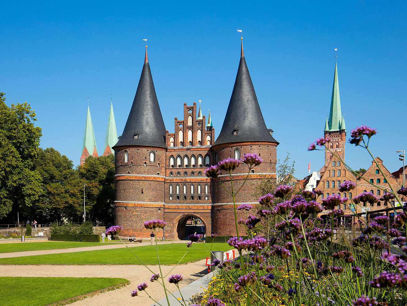 Holstentor Lübeck Holstentor in Lübeck mit blühenden Blumen im Vordergrund und blauem Himmel.