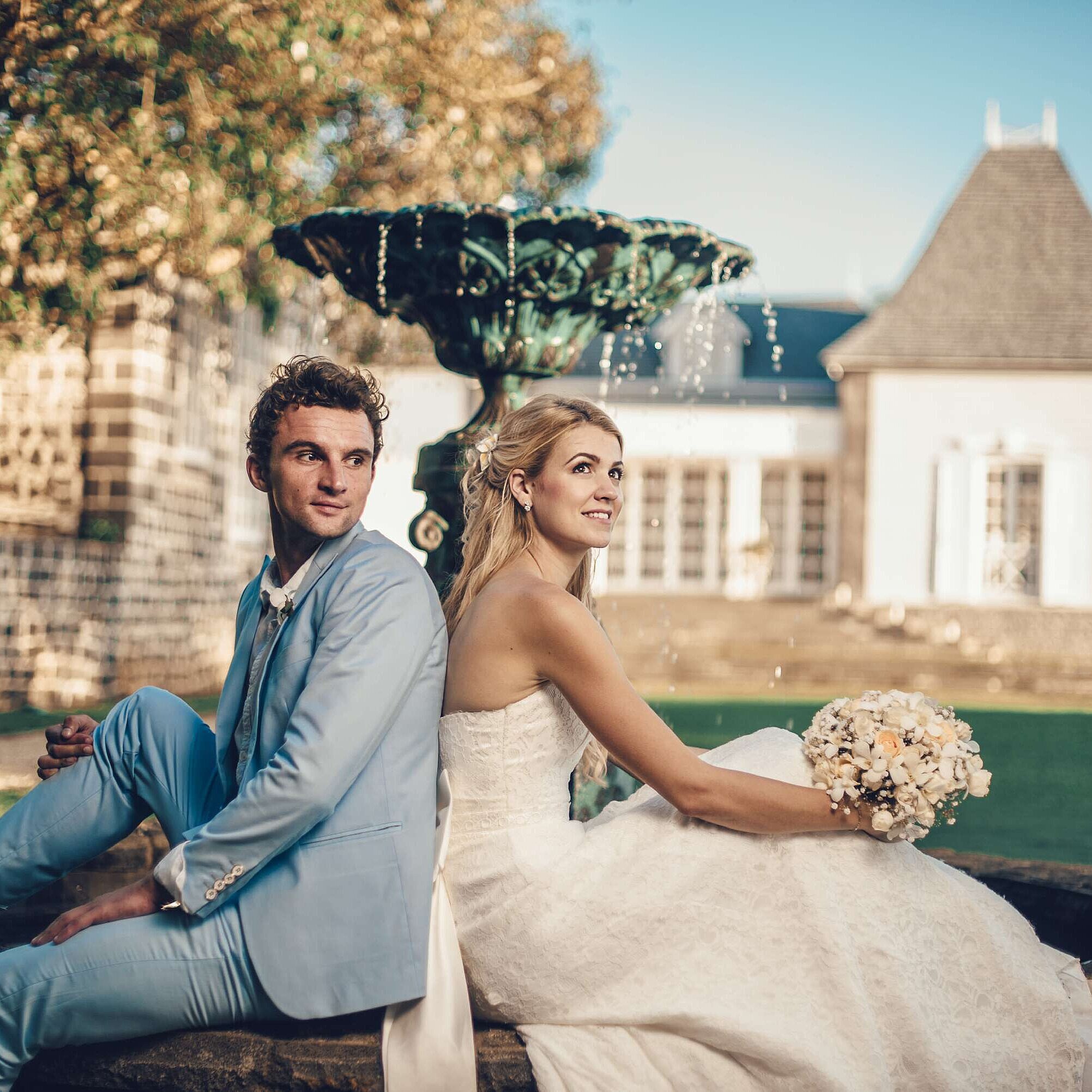Heiraten auf Mauritius Brautpaar sitzt Rücken an Rücken vor Brunnen und genießt romantische Hochzeitsmomente im Garten