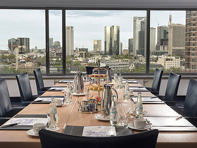 Skylounge Tagungsraum im Maritim Hotel Frankfurt mit Blick auf die Skyline. Eleganter Tisch, Getränke und Snacks für Meetings bereitgestellt.