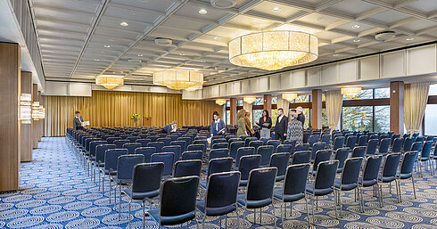 Saal Maritim Saal Maritim im Maritim Hotel Kiel, großer Konferenzraum mit Reihenbestuhlung, Kronleuchtern und Bühne, Personal bereitet den Raum vor.