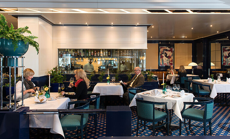 Restaurant "Sinfonie" Zwei Gäste genießen ihr Mittagessen im Restaurant des Maritim Magdeburg, mit Blick auf die Bar und die Küche im Hintergrund.