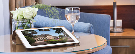 Zimmerdetail Gemütlicher Sitzbereich im Maritim Hotel Fulda mit Tablet, Glas Wasser und weißen Rosen auf einem Glastisch.
