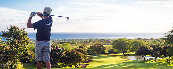 © Allen.G - AdobeStock.com Golfer beim Abschlag auf einem sonnigen Golfplatz mit Blick über das gepflegte Fairway und die Landschaft.