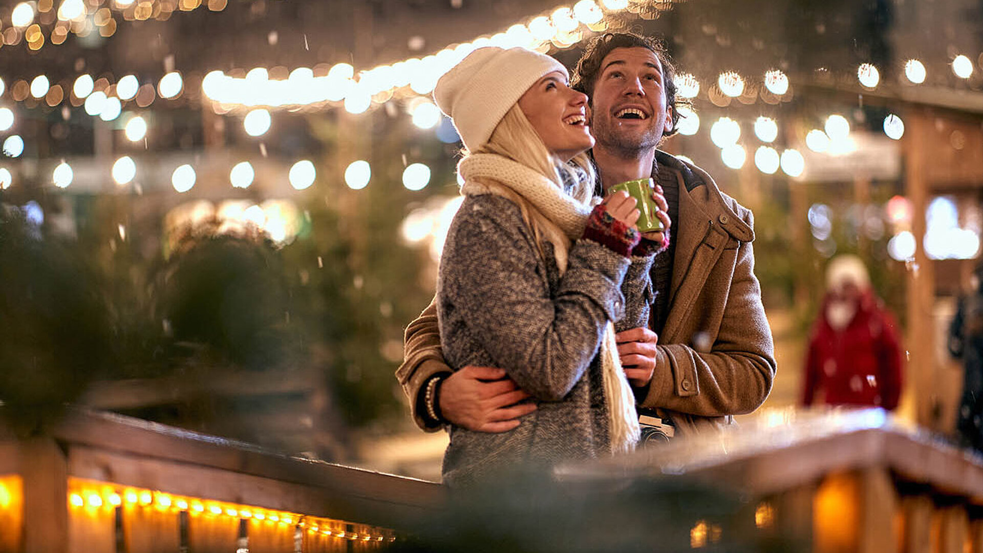 © luckybusiness - AdobeStock.com Paar genießt einen winterlichen Abend auf dem Weihnachtsmarkt, umgeben von warmen Lichtern und festlicher Stimmung.