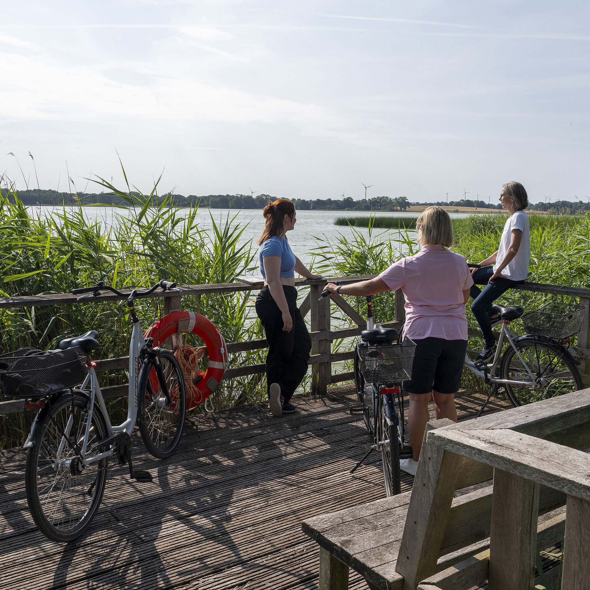 Fahrradtour Drei Frauen machen eine Pause auf einer Fahrradtour an einem Steg mit Blick auf den See beim Maritim Timmendorfer Strand.