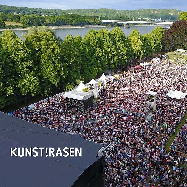 KunstRasen Open Air Große Menschenmenge beim Open Air Event KunstRasen am Rhein mit Bühne und Naturkulisse