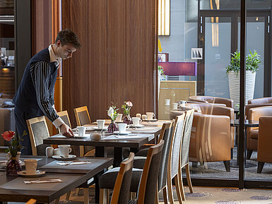 Restaurant Classico Mitarbeiter deckt einen Tisch im Restaurant Classico des Maritim Hotel Düsseldorf, umgeben von eleganter Einrichtung.
