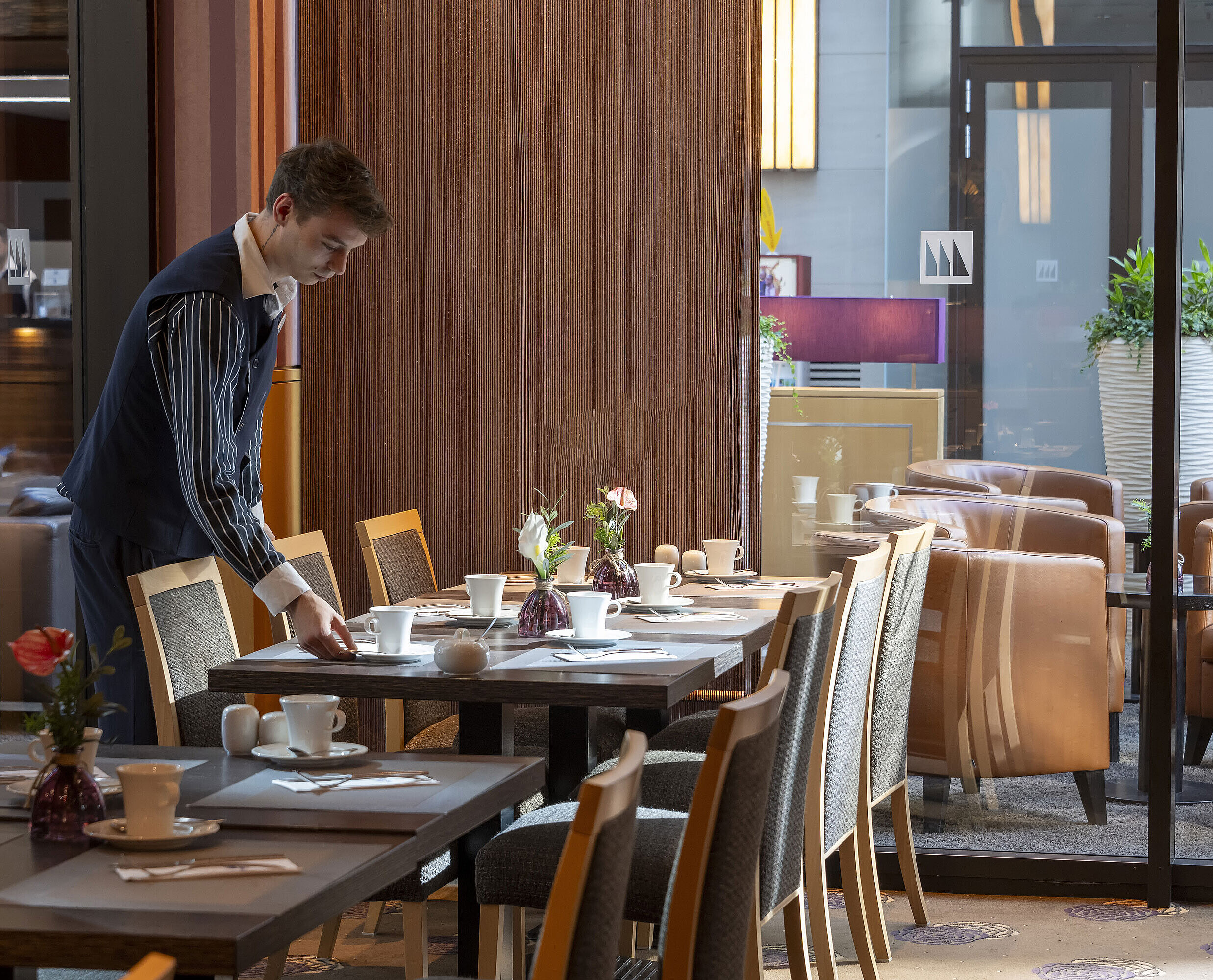 Restaurant Classico Mitarbeiter deckt einen Tisch im Restaurant Classico des Maritim Hotel Düsseldorf, umgeben von eleganter Einrichtung.
