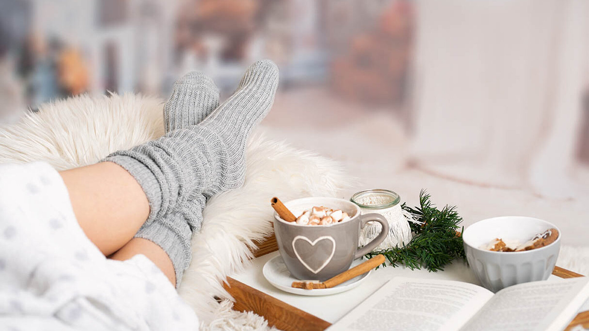 © Photo-SD - AdobeStock.com Person entspannt mit warmen Socken, Buch und einer Tasse heiße Schokolade auf einem gemütlichen Wintertablett.