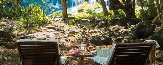 Picknick am Wasserfall Zwei Liegestühle mit Tisch im Grünen vor Wasserfall für entspannte Auszeit