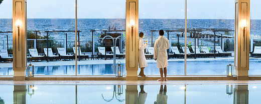 Schwimmbad Innenpool mit Meerblick im Maritim Seehotel Timmendorfer Strand, zwei Gäste in Bademänteln am Fenster.