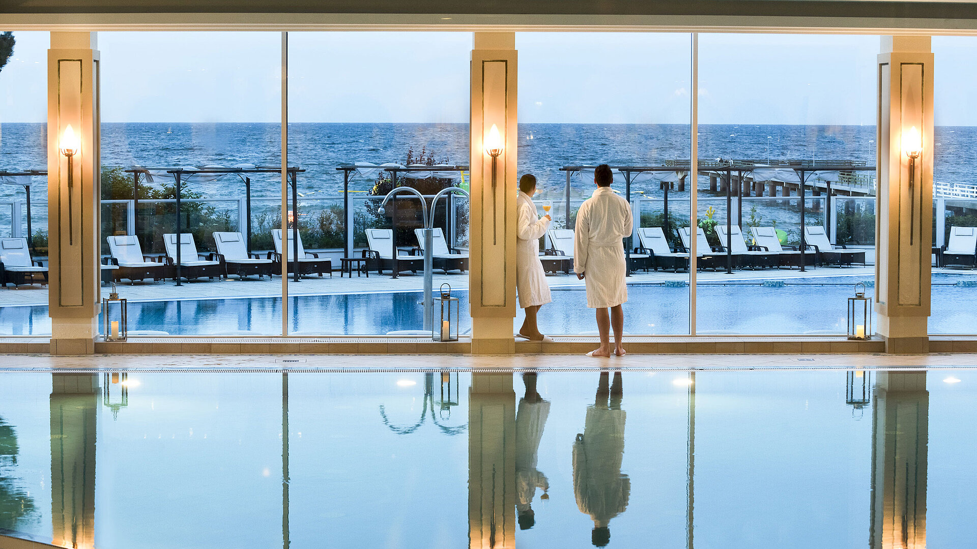 Schwimmbad Innenpool mit Meerblick im Maritim Seehotel Timmendorfer Strand, zwei Gäste in Bademänteln am Fenster.