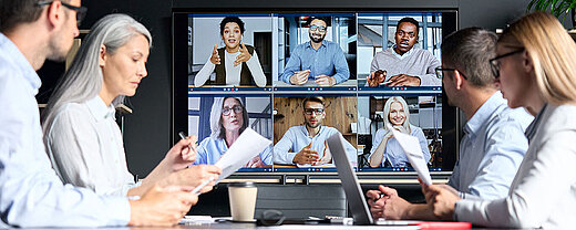 © insta photos - AdobeStock.com Geschäftsteam in Videokonferenz mit Kollegen auf großem Bildschirm
