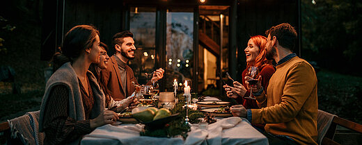 © La Famiglia - AdobeStock.com Freunde genießen gemeinsames Abendessen im Freien mit Lichterketten und Wein