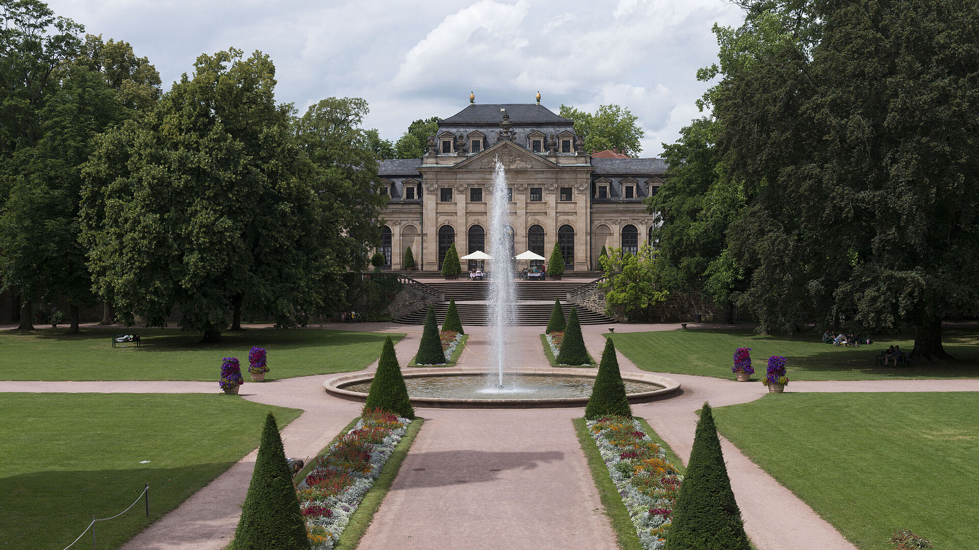 Außenansicht Die barocke Orangerie Fulda mit Schlossgarten, Springbrunnen und gepflegten Blumenbeeten im Vordergrund.