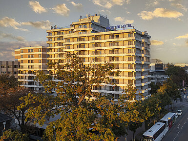 Außenansicht Außenansicht des Maritim Hotel Darmstadt bei Sonnenuntergang mit moderner Architektur und Bäumen im Vordergrund.